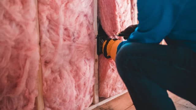 Worker installing insulation batts in a framed wall
